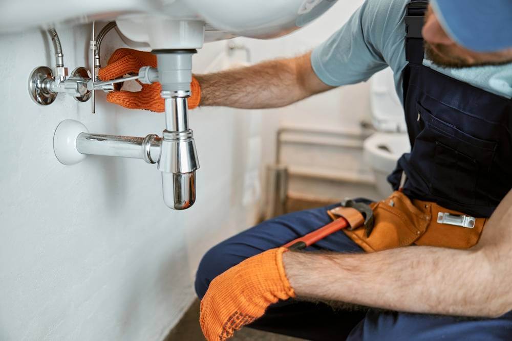 Plumber fixing pipe under sink performing plumbing repair work in Dubai.